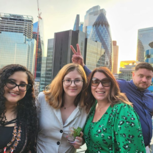 Three women standing on a rooftop terrace with skyscrapers in the background at AdTonos' July 'AudioSushi' Event