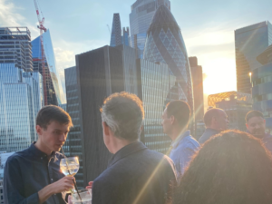 Men chatting and drinking outside with the London landmark Gherkin in the background at AdTonos' July 'AudioSushi' Event
